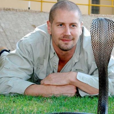 Associate Professor Bryan Fry flat on his stomach staring at a rearing cobra 